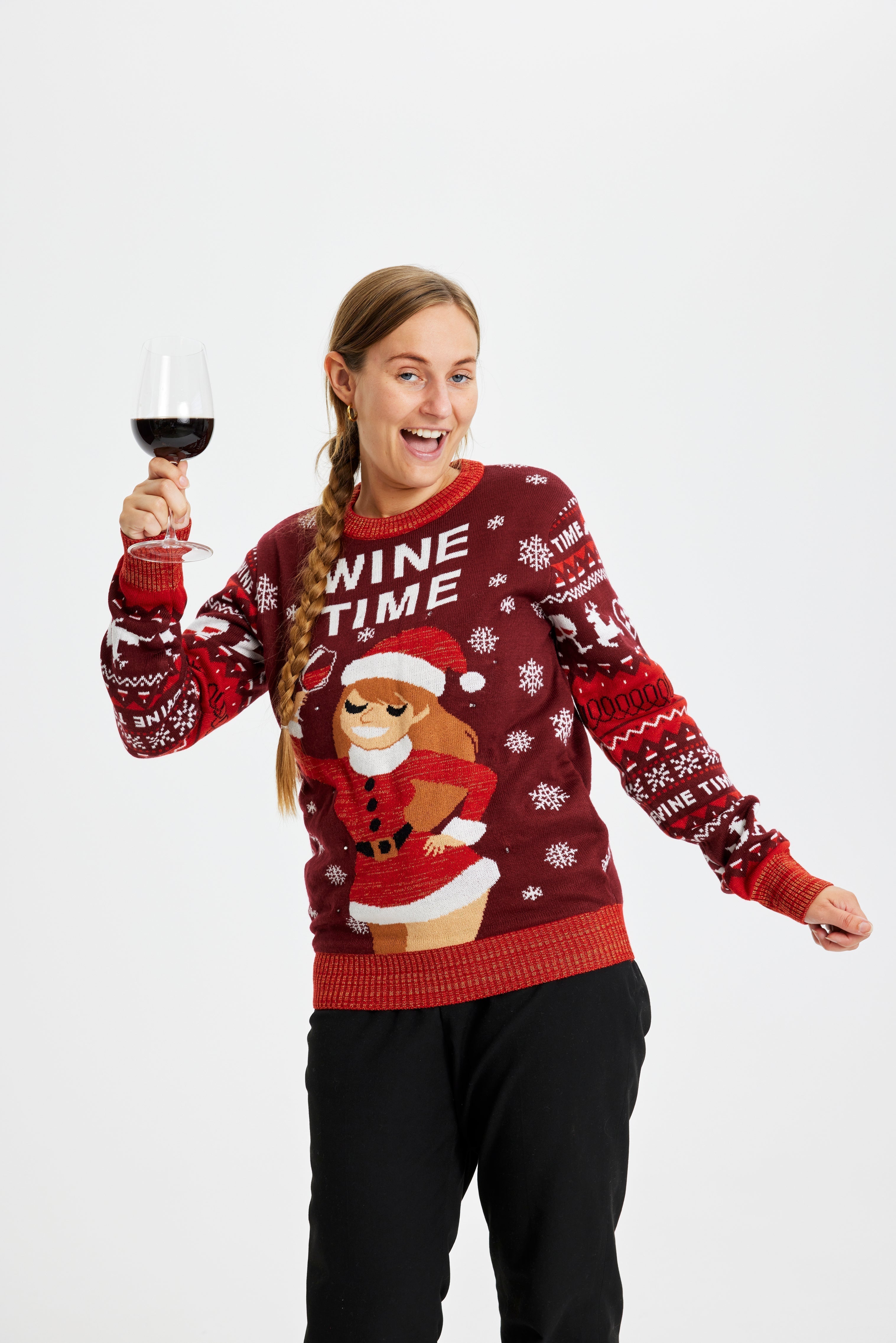 Una donna posa con un bicchiere di vino indossando un maglione rosso natalizio con la scritta